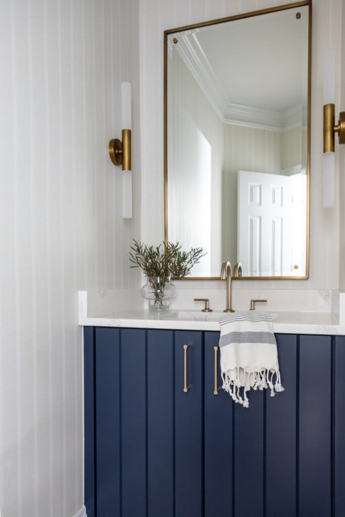 Bathroom with white shiplap walls, navy blue vanity, and brass framed mirror.