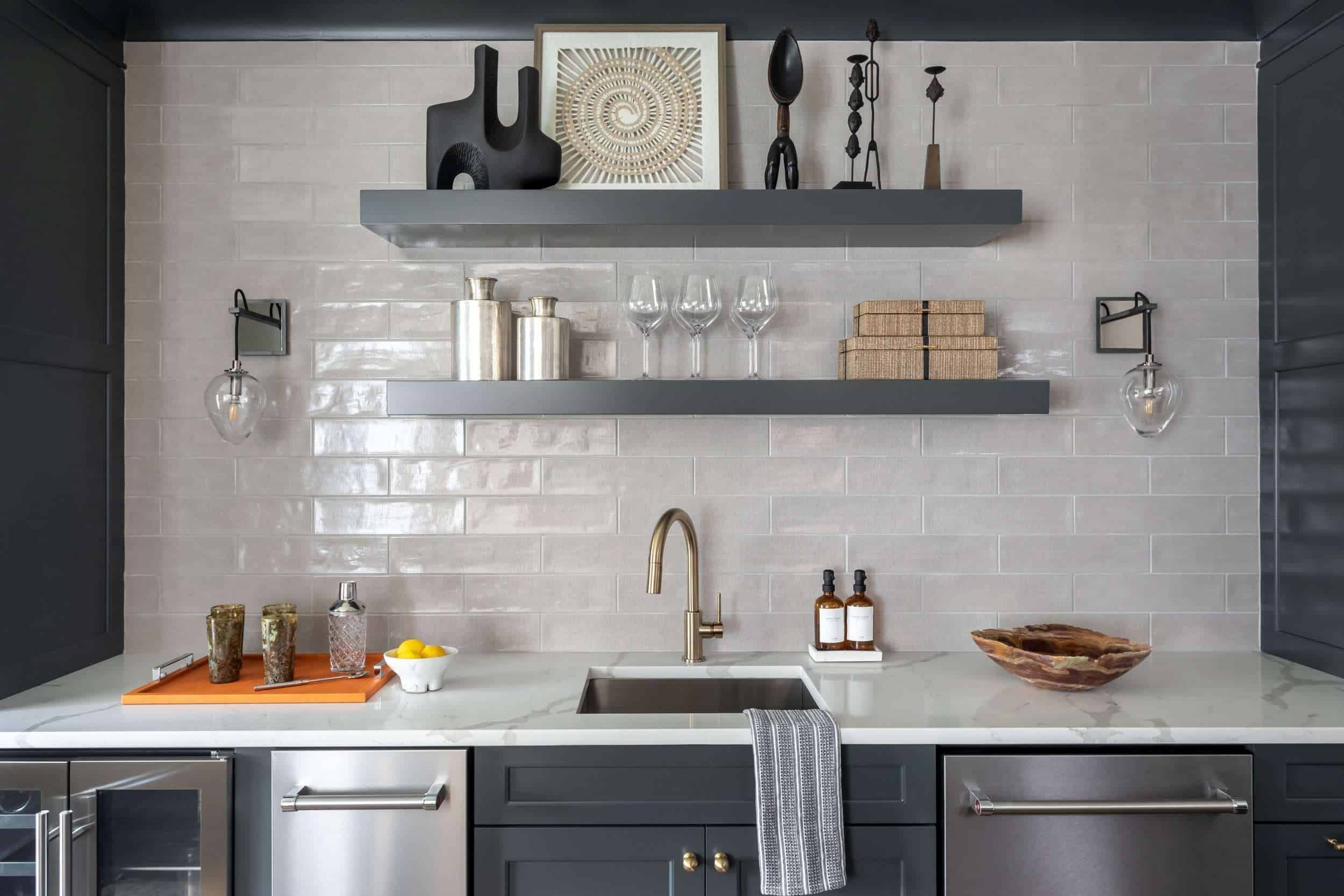 Sleek kitchenette with gray cabinets, white countertop, open shelves, and modern decor items. Features a stainless steel sink and appliances, with a minimalistic design.