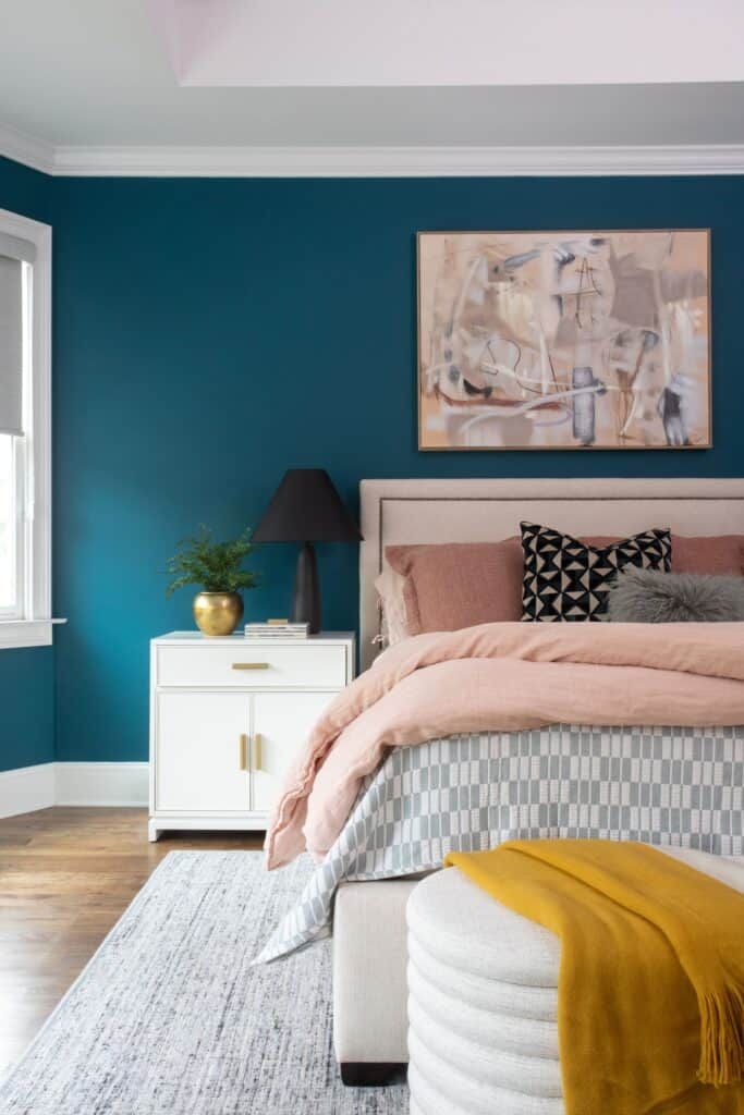 Bedroom with blue wall and bed with pink, gray, black, and white comforters and pillows.