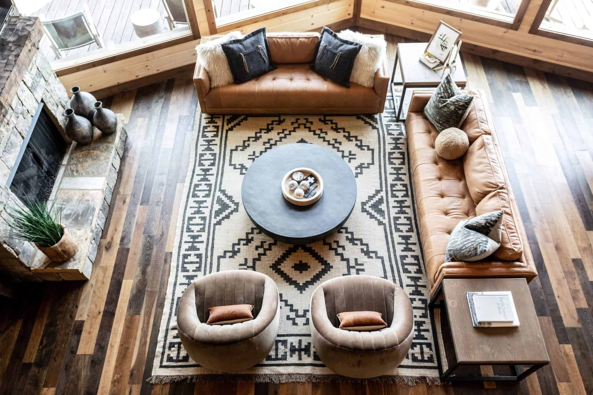 Aerial view of rustic living room with orange leather couches, velvet chairs, and tribal rug.