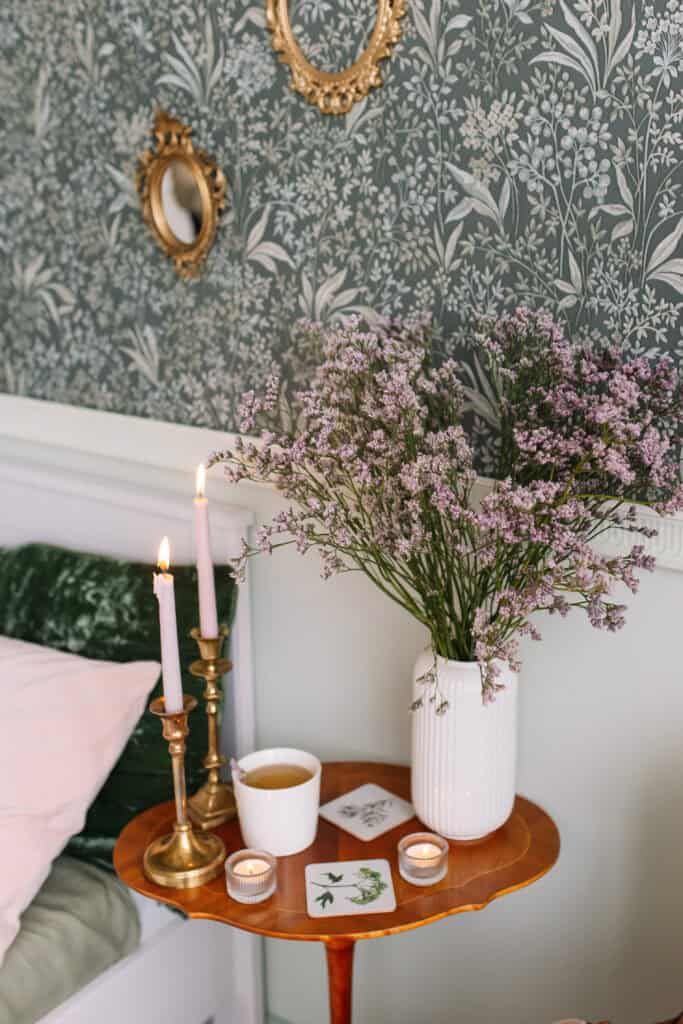 Green and white dainty flower and botanical wallpaper with gold round mirrors and flowers and candles sitting on a side table. 