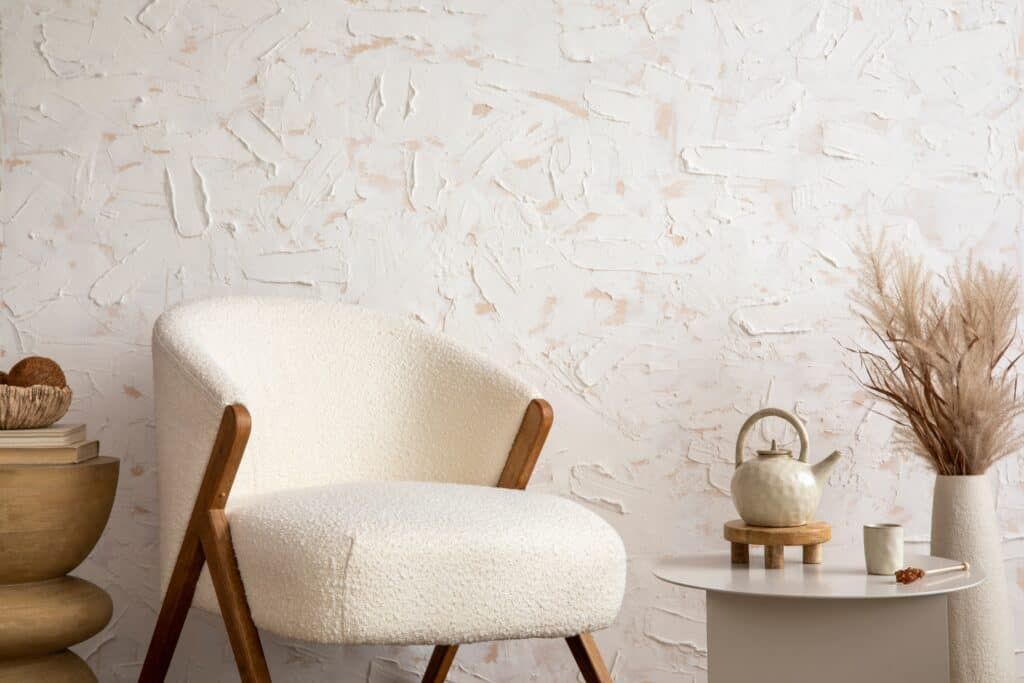 White and beige wallpaper with textured smears of raised paint in random patterns. White chair and decor items sit in front. 