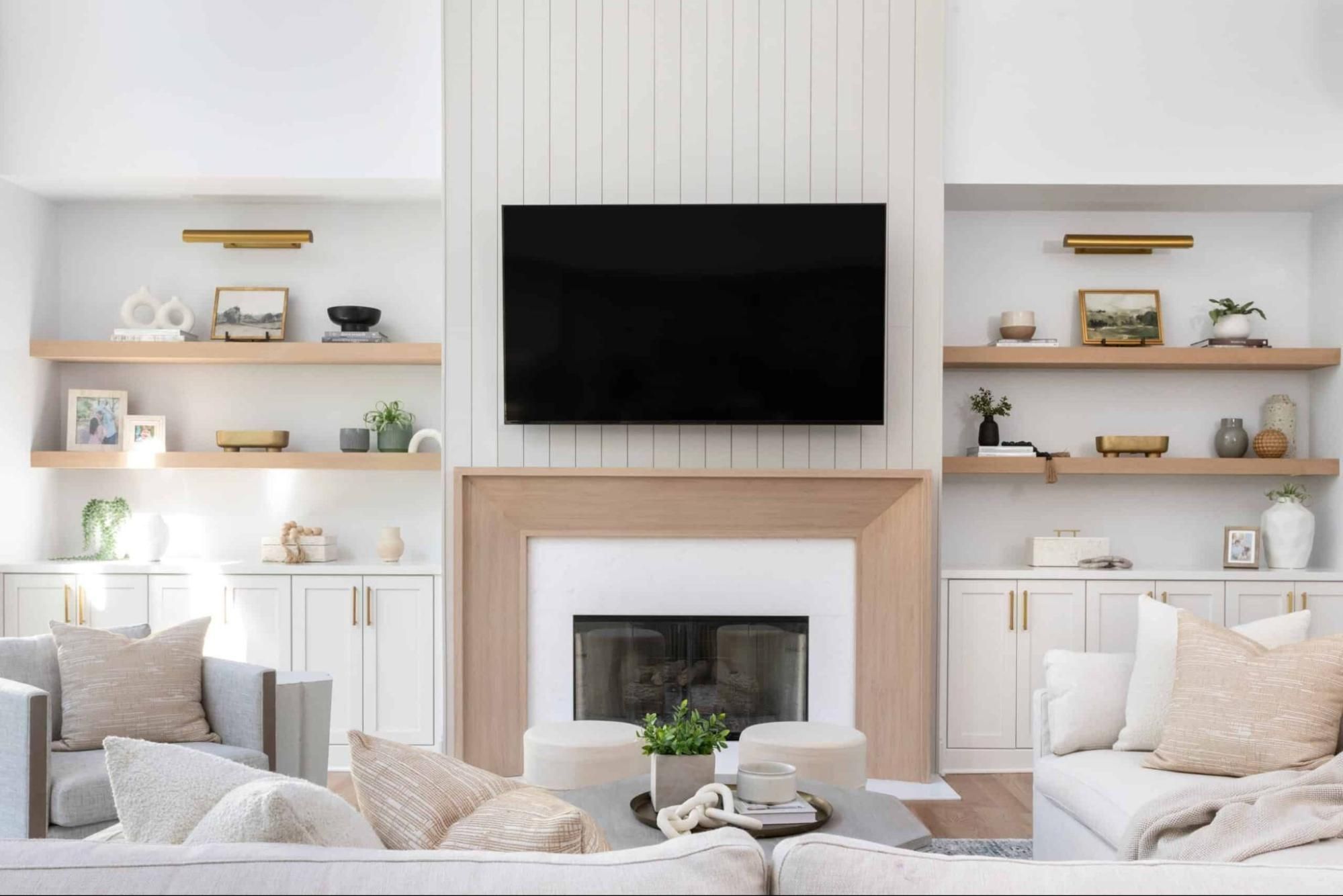 Living room with wood surround fireplace, natural wood shelving, and gray paneling. 