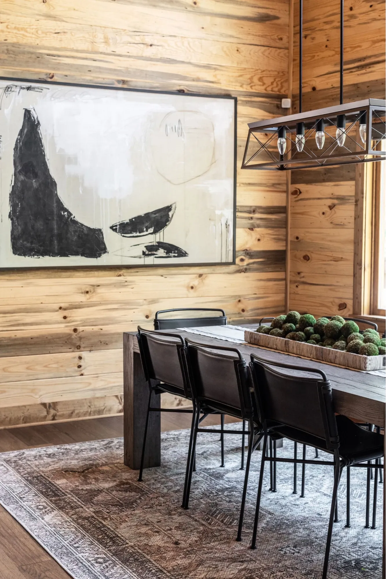 Rustic contemporary dining room with wood plank walls, oversized abstract artwork, industrial pendant lighting, and a reclaimed wood dining table.