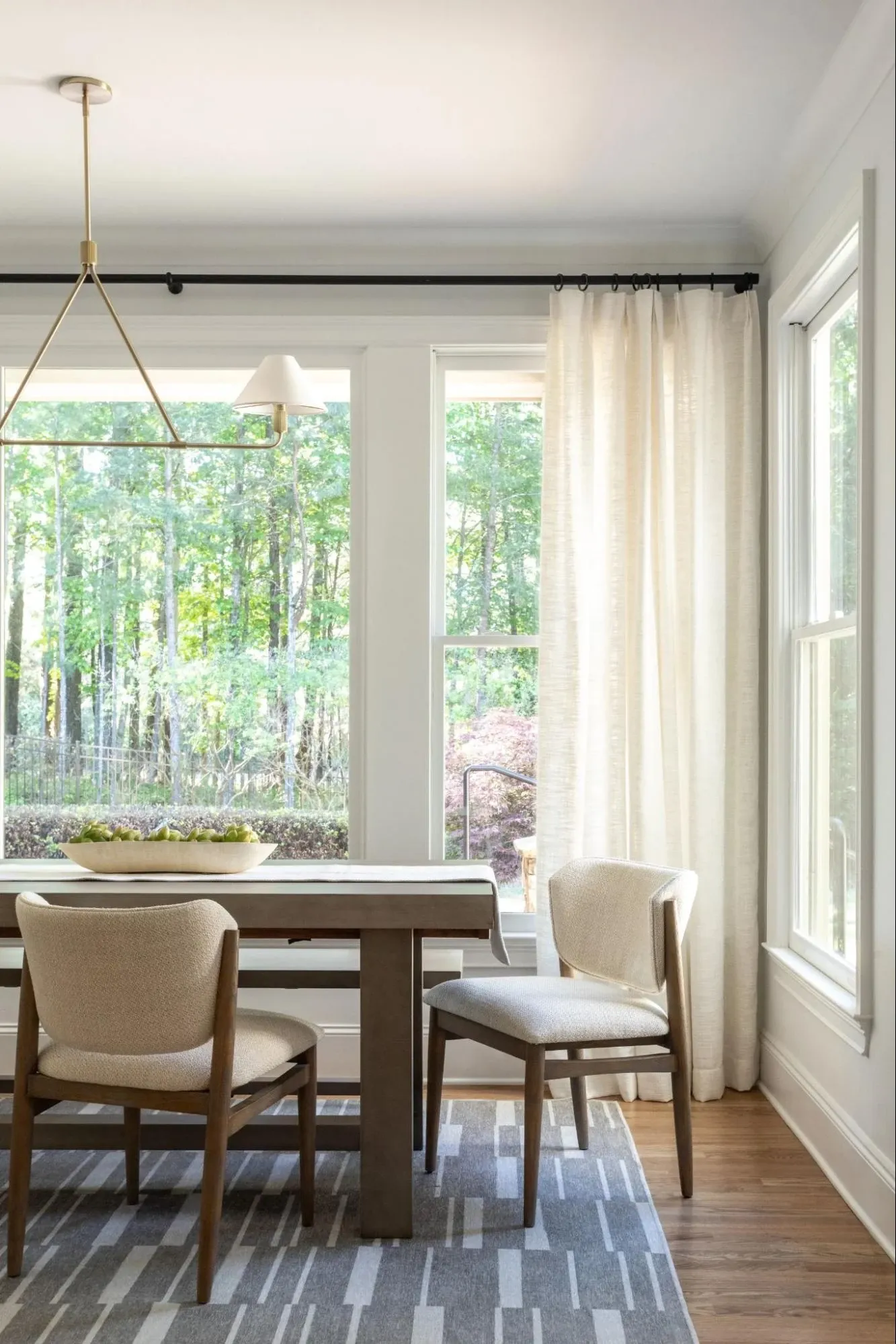 Luxury dining room with custom drapery, upholstered dining chairs, layered lighting, and a contemporary wood dining table.