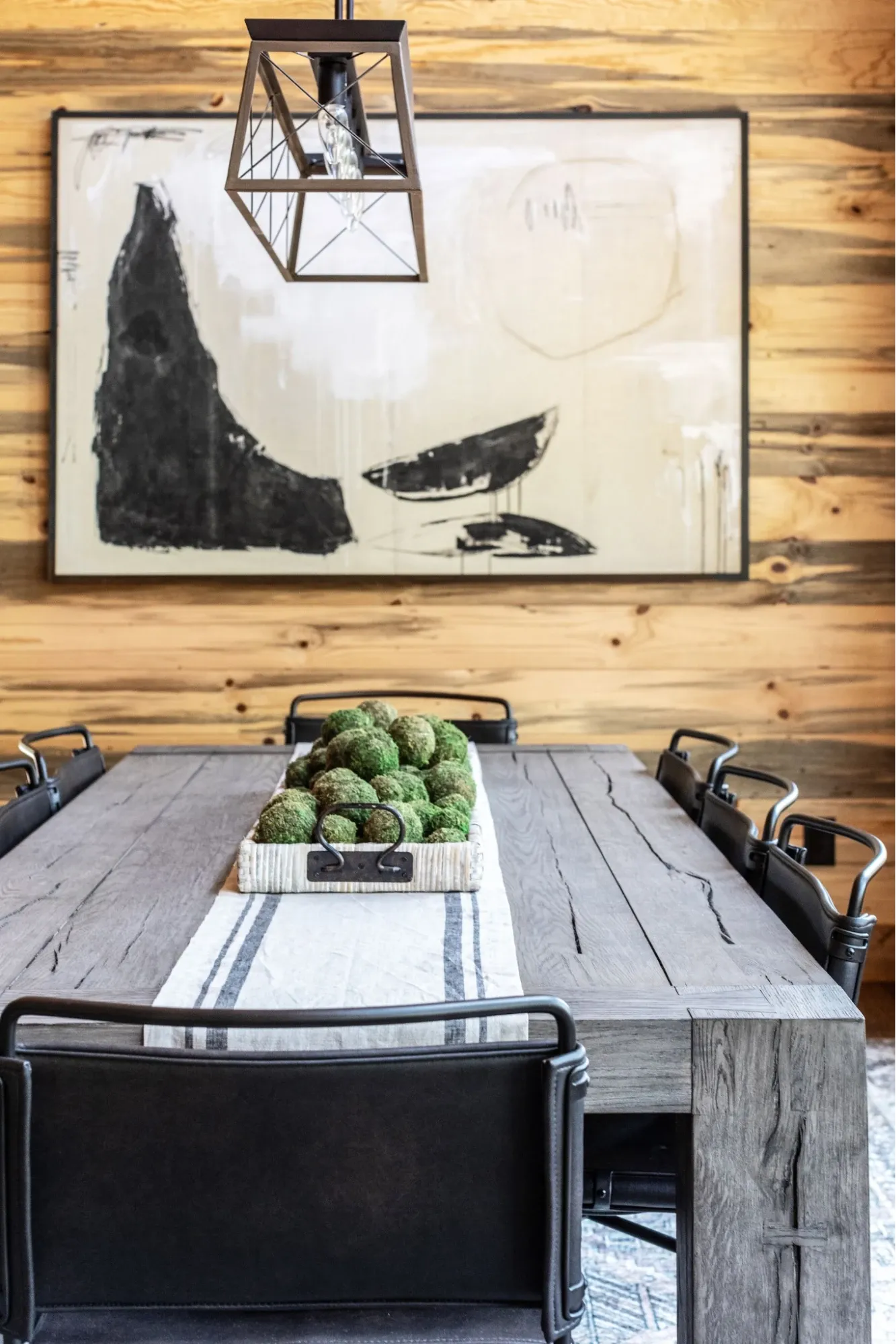Rustic luxury dining room with a reclaimed wood dining table, industrial dining chairs, abstract artwork, and geometric pendant lighting.
