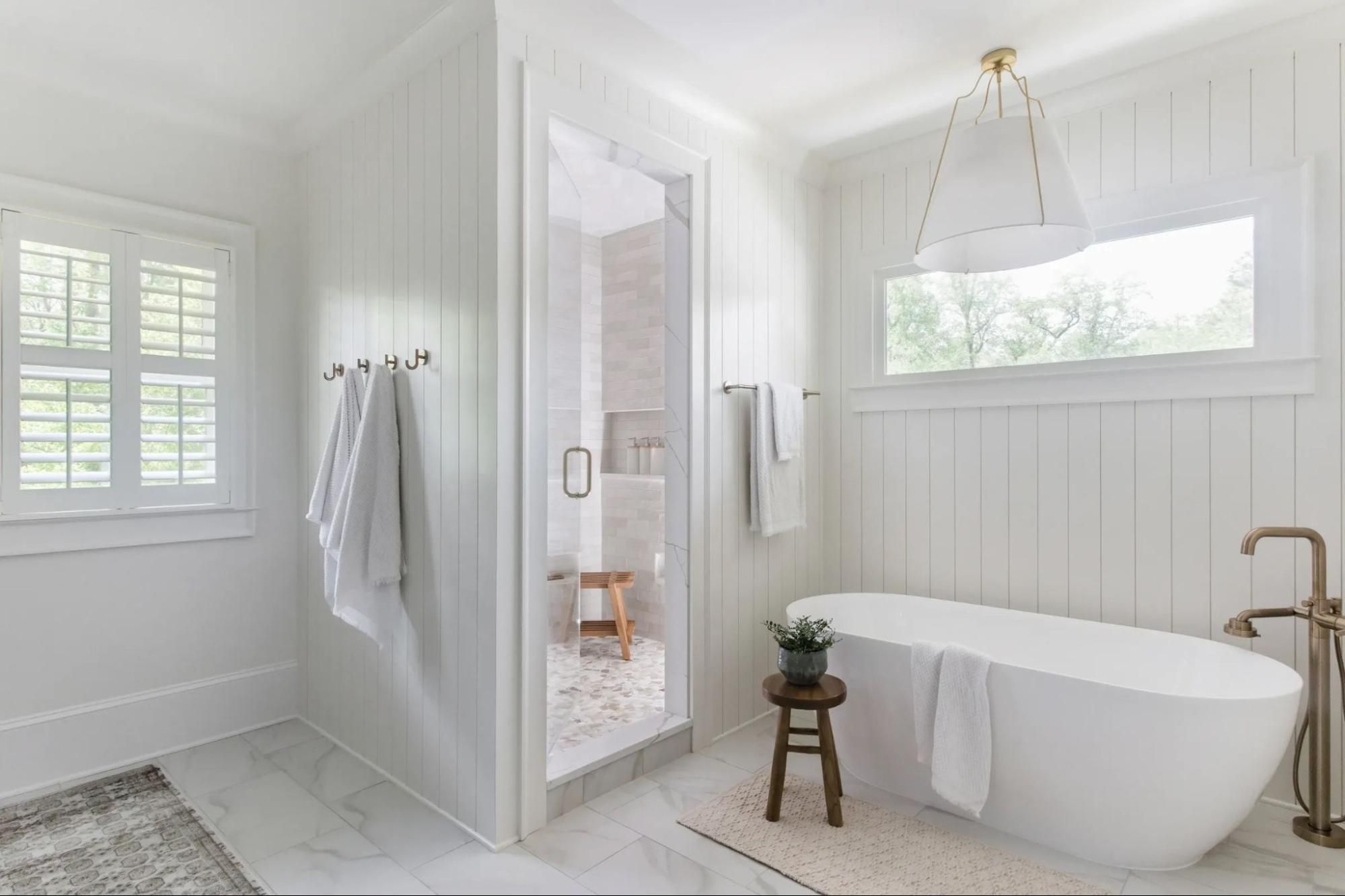 White bathroom with free standing tub, walk-in shower and lampshade chandelier. 