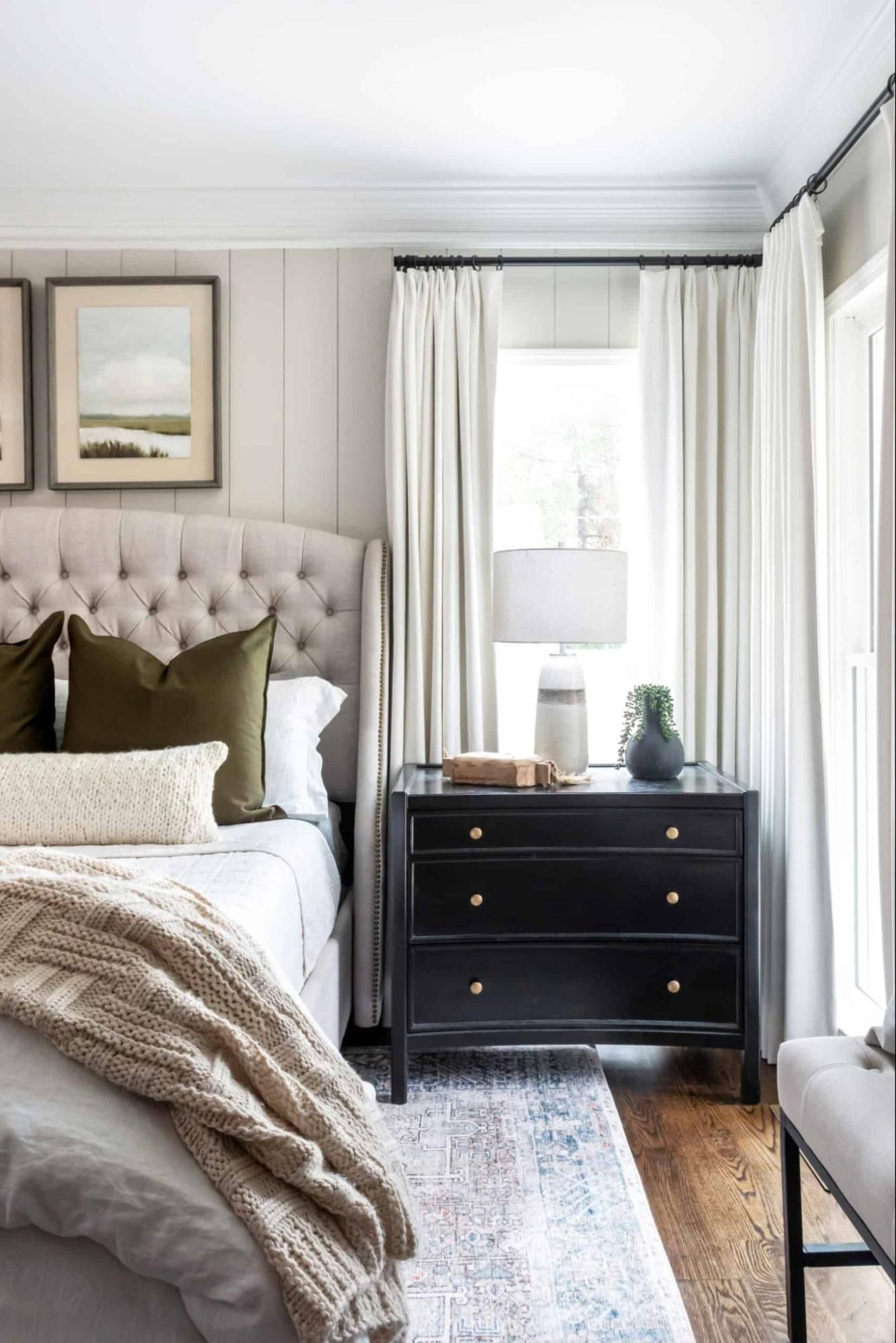 Bedroom with black dresser, green pillows, cottage-core decor, and greige walls. 