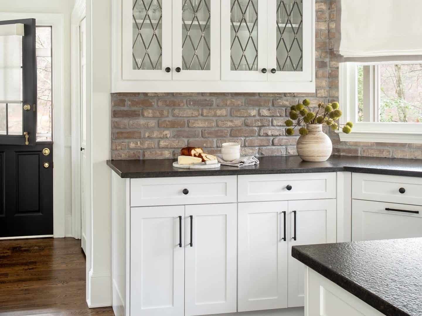 A modern classic interior design kitchen with refurbished Dutch door, brick veneer backsplash, and honed black granite countertop.