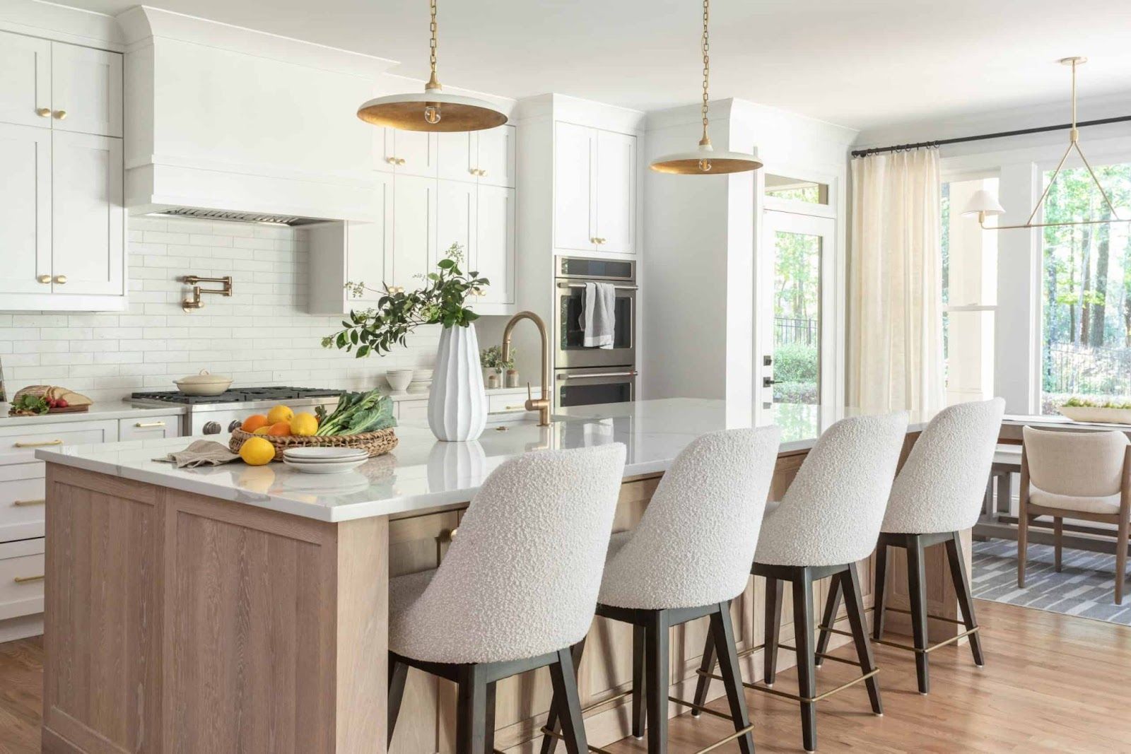 White kitchen with boucle swivel chairs, gold hardware, and a white and wood kitchen island.