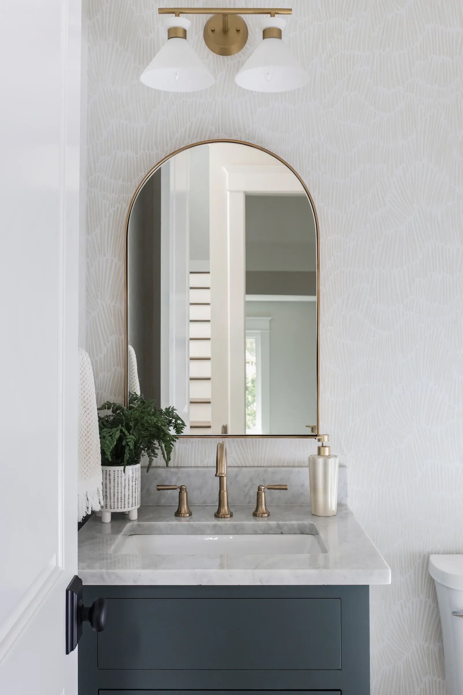 Bathroom with brushed brass faucet and arched mirror.